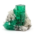Ejemplar natural de cristal de esmeralda de color verde intenso, con una estructura prismática hexagonal prominente rodeada por una matriz de cristales de roca blanquecinos